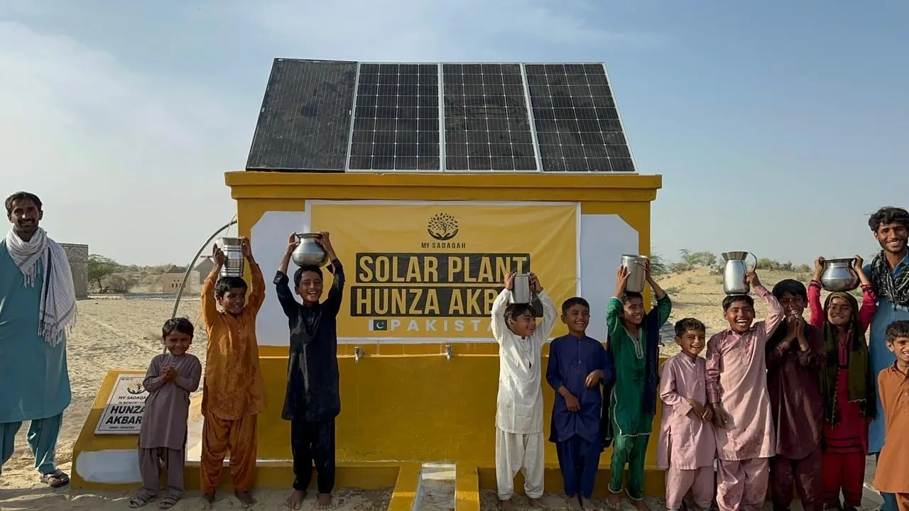 Children hold up their water pots in front of the My Sadaqah Solar Plant Hunza Akbar